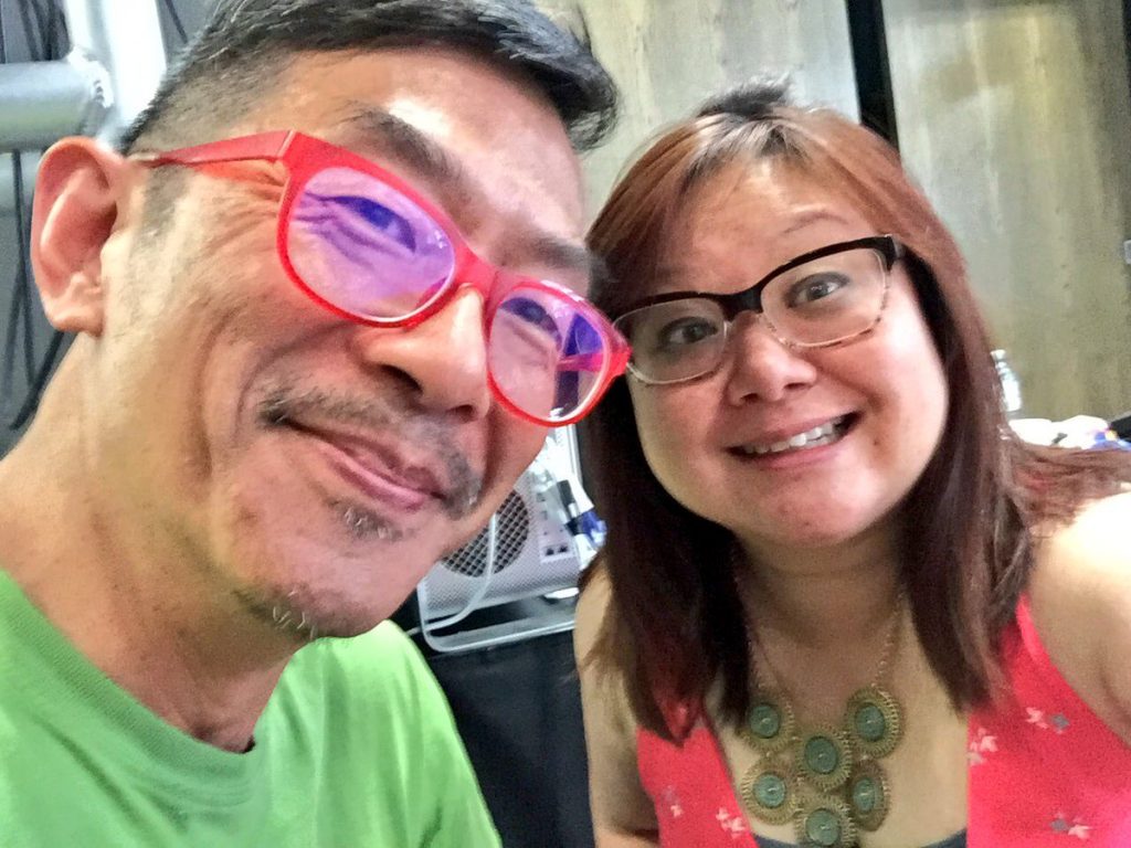 Picture of older Asian man in distinctie glasses and middle-aged Asian woman in black glasses, both smiling